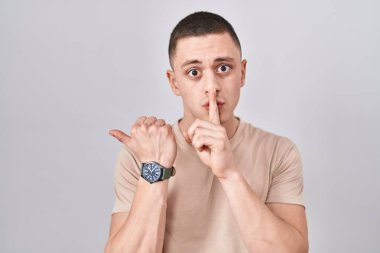 İzole edilmiş arka planda duran genç adam sessiz olmak istiyor. Parmaklarıyla dudaklarını yana doğru gösteriyor. sessizlik ve gizli konsept. 