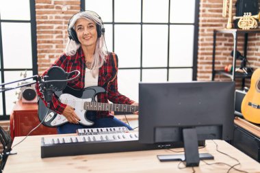 Middle age grey-haired woman musician playing electrical guitar at music studio