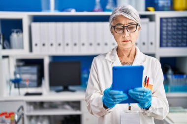 Orta yaşlı, gri saçlı kadın bilim adamı. Laboratuvarda çalışan dokunmatik ped kullanıyor.