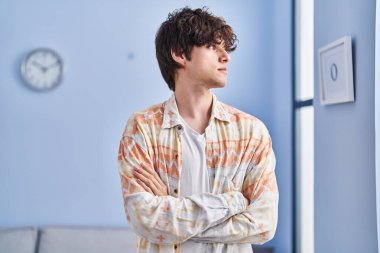 Ciddi bir ifadeyle ve kollarını kavuşturarak evde dikilen İspanyol genç bir adam.