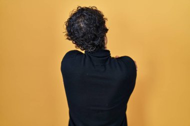 İspanyol adam sarı arka planda dikilip kendine sarılıyor mutlu ve pozitif bir şekilde. Sevgi ve özgüven. 