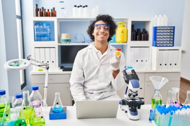 Genç İspanyol adam bilim adamı üniforması giyiyor. Laboratuvarda idrar testi tüpünü inceliyor.