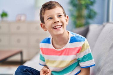 Sarışın çocuk evdeki kanepede kendinden emin bir şekilde oturuyor.