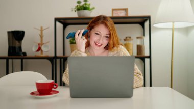 Genç kızıl saçlı kadın evde akıllı telefondan laptopla sesli mesaj dinliyor.