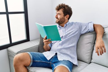 Evdeki kanepede oturmuş kitap okuyan genç bir İspanyol..