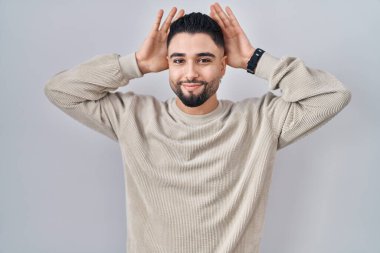 Soyutlanmış arka planda duran genç yakışıklı adam avuçlarında alaycı ve şüpheci bakışlarla tavşan kulağı hareketi yapıyor. Paskalya tavşanı konsepti. 