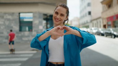 Young woman smiling confident doing heart gesture with hands at street