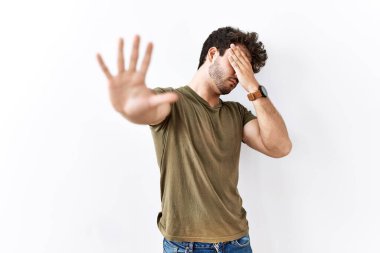 İspanyol bir adam, izole edilmiş beyaz arka planda duruyor. Gözleri ellerle kaplıyor ve üzgün ve korku dolu bir ifadeyle jesti durduruyor. utangaç ve olumsuz kavram. 