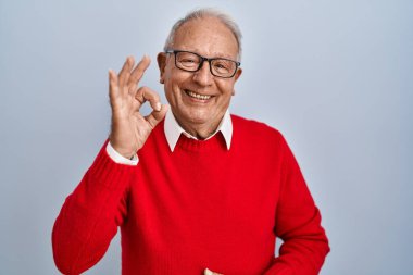 İzole edilmiş arka planda gri saçlı yaşlı adam gülümsüyor ve el ve parmaklarıyla 