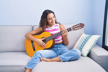 Evdeki kanepede oturmuş klasik gitar çalan genç ve güzel bir İspanyol kadın.