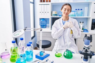 Laboratuvarda çalışan esmer bir kadın. Elleri göğsünde, gözleri kapalı gülümsüyor ve yüzünde minnet dolu bir jest var. sağlık kavramı. 