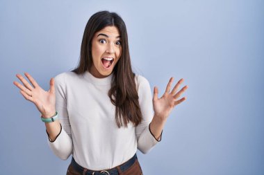 Mavi arka planda duran genç esmer kadın çılgın ve başarıyı kollarını kaldırıp heyecanla haykırarak kutluyor. Kazanan konsept 