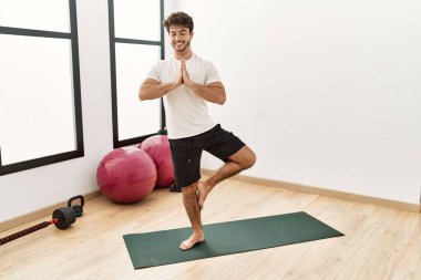 Genç İspanyol adam gülümsüyor spor merkezinde yoga antrenmanı yapıyor.
