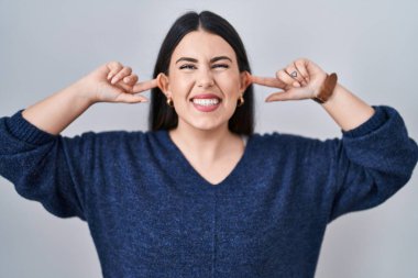 Genç esmer kadın izole edilmiş arka planda duruyor. Gülümsüyor, kulakları parmaklarıyla çekiyor. Komik bir jest. deneme sorunu 