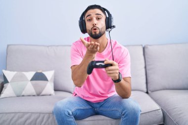 İspanyol asıllı genç adam video oyunu oynuyor kanepede oturmuş kameraya bakıyor ve havada bir öpücük savuruyor sevimli ve seksi. aşk ifadesi. 