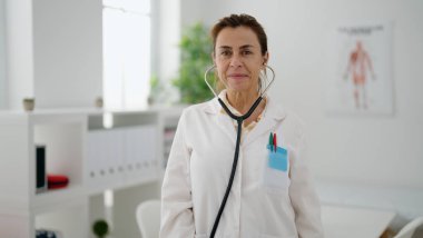 Klinikte dikilen orta yaşlı İspanyol kadın doktor üniforması giyiyor.