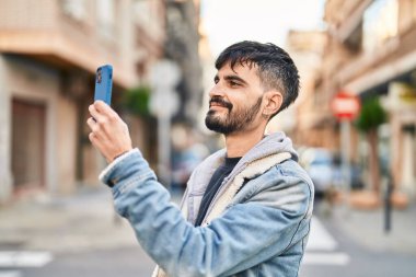 Genç İspanyol adam kendinden emin gülümsüyor. Akıllı telefondan sokak fotoğrafı çekiyor.