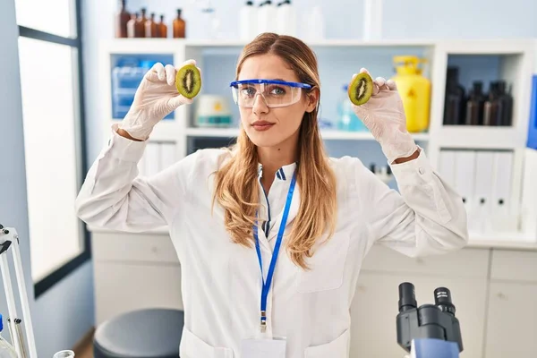 Young blonde scientist woman working with food at laboratory clueless and confused expression. doubt concept.