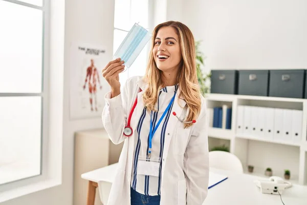 Young Blonde Woman Wearing Doctor Uniform Holding Medical Mask Clinic — Stock Photo, Image