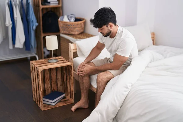 Young Hispanic Man Suffering Knee Injury Sitting Bed Bedroom —  Fotos de Stock