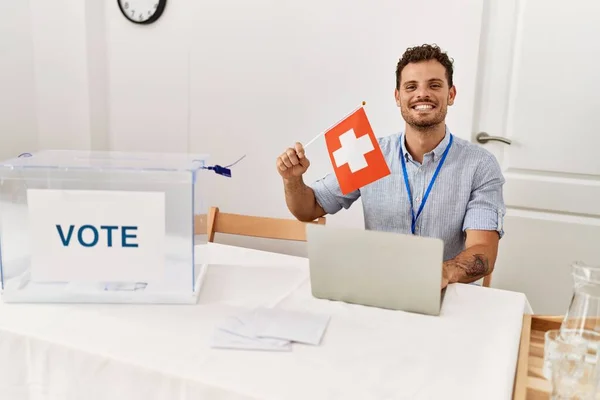 Joven Hispano Sonriendo Confiado Sosteniendo Bandera Suiza Trabajando Colegio Electoral — Foto de Stock