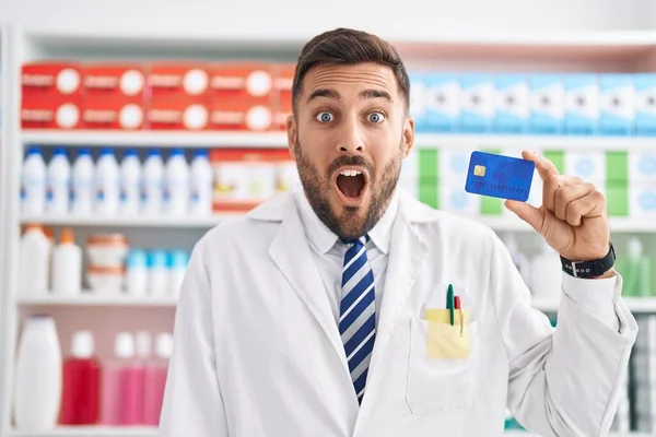 Handsome Hispanic Man Working Pharmacy Drugstore Holding Credit Card Scared — Stock Photo, Image