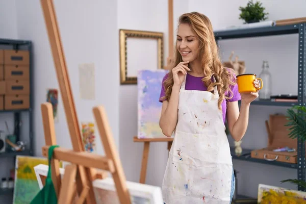 年轻的金发女艺术家微笑着自信地在艺术工作室喝咖啡 — 图库照片