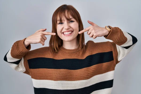 孤立した背景の上に縞模様のセーターを着て若い美しい女性は陽気に笑い 指の歯と口で指しています 歯の健康の概念 — ストック写真