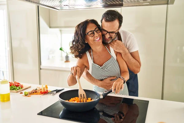 Orta yaşlı İspanyol çift gülümsüyor. Kendilerine güveniyorlar ve mutfakta yemek pişiriyorlar.