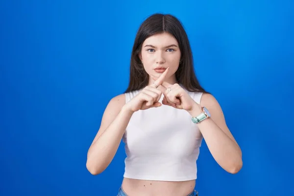 年轻的高加索女人站在蓝色背景下 用手指交叉表示拒绝 做阴性手势 — 图库照片
