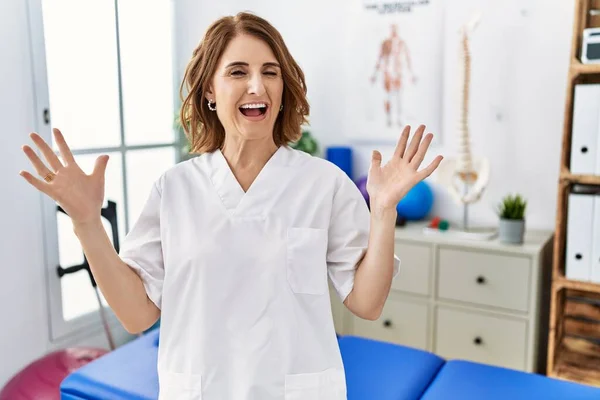 在疼痛康复诊所工作的中年理疗师女人兴奋地举起双臂 睁开眼睛尖叫 庆祝自己的成功 获奖者概念 — 图库照片