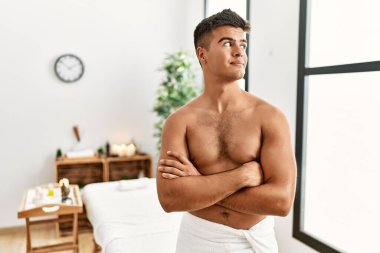 Genç İspanyol adam spa merkezinde üstsüz duruyor. Gülümsüyor, yan tarafa bakıyor ve düşünüyor.. 