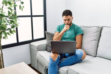 Sakallı genç yakışıklı adam evdeki kanepede oturup hasta hissediyor ve soğuk algınlığı veya bronşitin belirtisi olarak öksürüyor. sağlık hizmeti kavramı. 