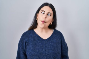 Genç esmer kadın izole arka planda duruyor. Dudaklarıyla balık suratı yapıyor. Çılgınca ve komik bir jest. Komik ifade. 