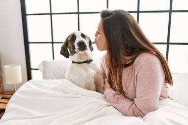 Genç bir kadın yatak odasında öpüşüyor ve köpeğe sarılıyor.