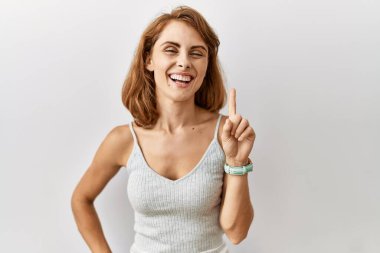 Güzel, beyaz bir kadın izole edilmiş arka planda duruyor. Bir numarayı işaret ediyor ve gülümsüyor. Kendinden emin ve mutlu.. 