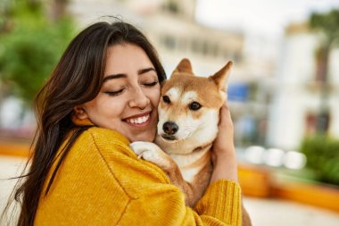 Güzel genç bir kadın parkta mutlu Shiba Inu köpeğine sarılıyor.