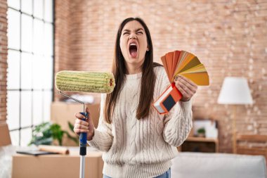 Genç esmer kadın paten boyacısı ve boya örnekleri tutuyor kızgın ve kızgın çığlıklar atıyor öfkeyle ve öfkeyle bağırıyor öfkeyle yukarı bakıyor. 