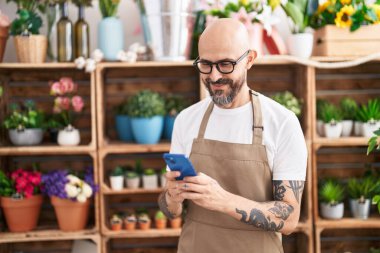 Çiçekçiye akıllı telefon kullanarak gülümseyen kel bir çiçekçi.