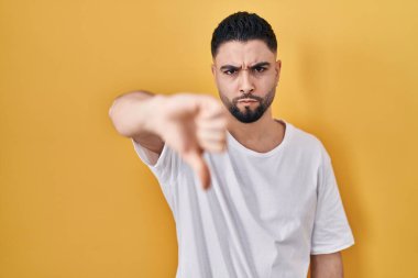 Sarı arka plan üzerine gündelik tişört giyen genç yakışıklı adam mutsuz ve kızgın görünüyor. Reddedilmiş ve olumsuz. kötü ifade. 