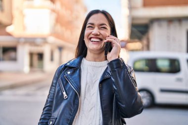 Gülümseyen genç bir kadın caddedeki akıllı telefondan konuşuyor.
