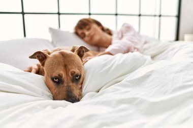 Beyaz bir kadın yatak odasında köpekle yatakta yatıyor.