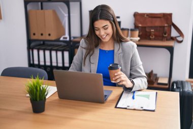 Genç, güzel İspanyol iş kadını. Laptop kullanıyor. Ofiste kahve içiyor.