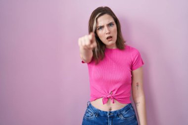 Blonde caucasian woman standing over pink background pointing displeased and frustrated to the camera, angry and furious with you 