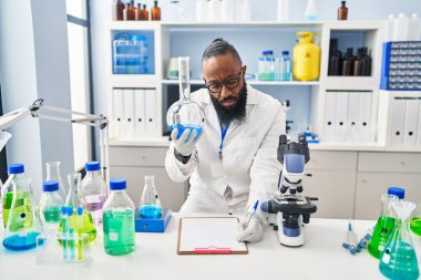 Bilim adamı üniforması giyen genç Afro-Amerikan adam laboratuarda test tüpü tutuyor.