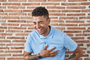 Brezilya 'lı genç adam tuğla duvarın üzerinde durmuş gülümsüyor ve kahkahalarla gülüyor.. 