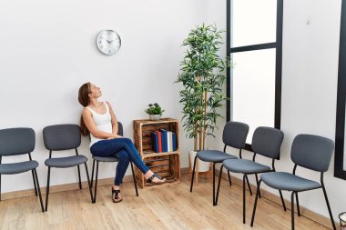 Bekleme odasında sandalyede oturan beyaz, sıkıcı genç bir kadın.