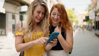 Two women standing together using smartphone at street