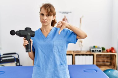 Sağlık merkezinde terapi tabancası tutan güzel beyaz bir kadın. Kızgın suratlı, olumsuz işaretli, baş parmakları aşağıda, reddedilme kavramından hoşlanmadığını gösteren. 