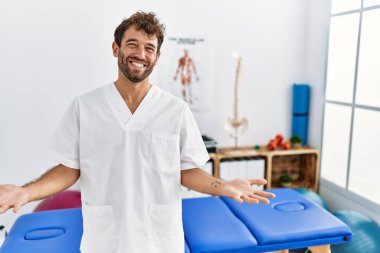 Genç, yakışıklı fizyoterapist, ağrı kesici kliniğinde çalışıyor. Kollarını açıp gülümsüyor. Dostça karşılama, olumlu ve kendinden emin selamlar. 